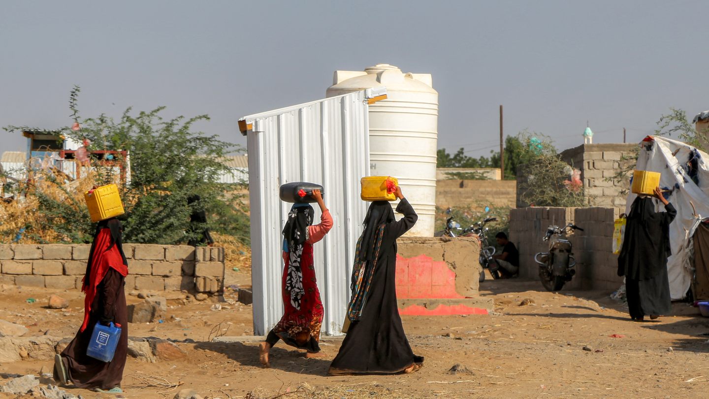 Women carry jerrycans of water through a camp for people displaced by conflict in Yemen's Khokha district, south of Hodeida, 4 January 2025 (Khaled Ziad/AFP)
